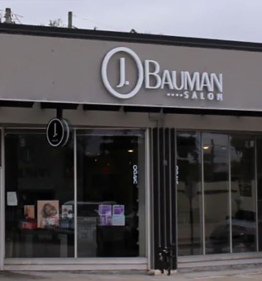 Storefront of j. bauman salon featuring a modern signage with large circle motif above glass windows displaying products and promotions.