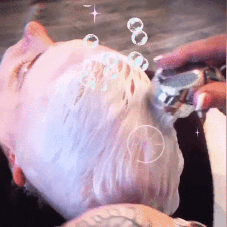 A person is getting their hair dyed in a bright, sparkling silver color, with a close-up view showing the application of dye on the scalp using a brush.