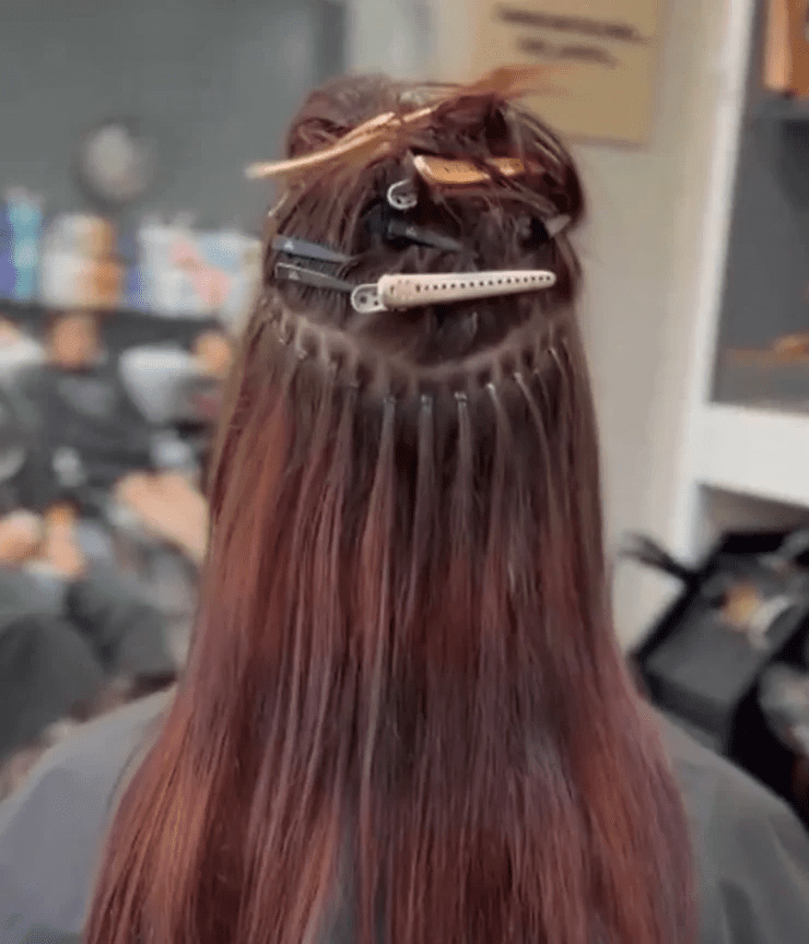 Back view of a person's head at a hair salon, showing long brown hair sectioned with several clips for styling, in a professional setting.