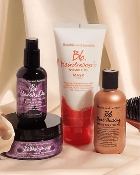 A collection of bumble and bumble hair care products, including invisible oil mask, curl primer, scalp detox, and bond-building repair treatment, artistically arranged with a soft beige background.