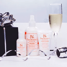 A festive display featuring haircare products with a glass of champagne, a wrapped gift box, and ribbon on a white surface.