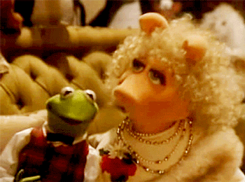 A gif of kermit the frog and miss piggy from the muppets, interacting in a warmly lit setting, showcasing miss piggy talking animatedly while kermit listens.