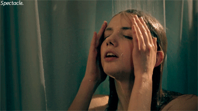 A woman enjoys rinsing her face with water in the shower, eyes closed and hands on her forehead, behind a semi-transparent shower curtain. the word "spectacle." appears at the bottom.