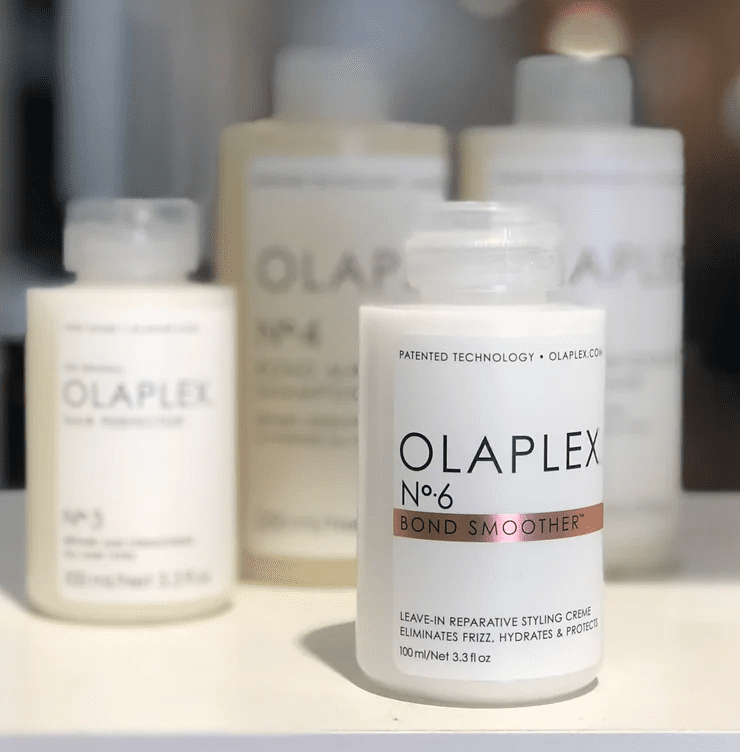 A close-up of a bottle of olaplex no. 6 bond smoother hair product, with additional bottles blurred in the background. the label highlights its leave-in reparative styling crème functions.