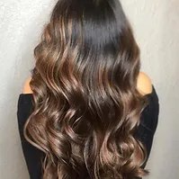 A woman with shiny, wavy chestnut brown hair cascading down her back, highlighting various shades of brown with subtle, natural-looking highlights.