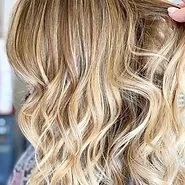 Close-up of a person's wavy, blonde hair showcasing various shades and highlights. the focus is on the texture and color depth of the hair.