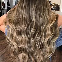A woman's long, wavy hair with beautiful balayage highlights transitioning from brown at the roots to blonde at the tips.