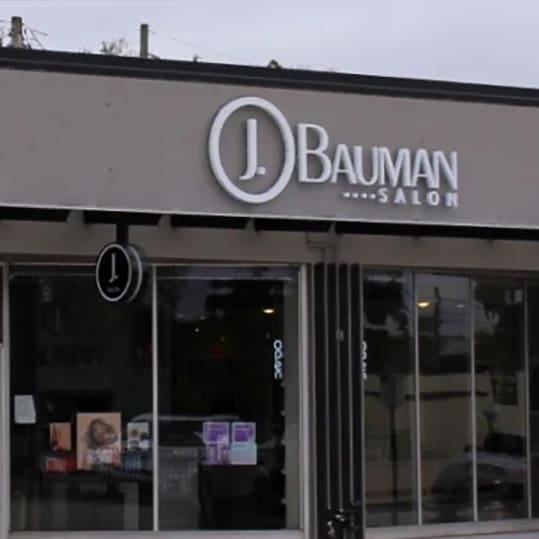 The facade of j. bauman salon, showing its signage above the entrance, with large glass windows displaying beauty products.