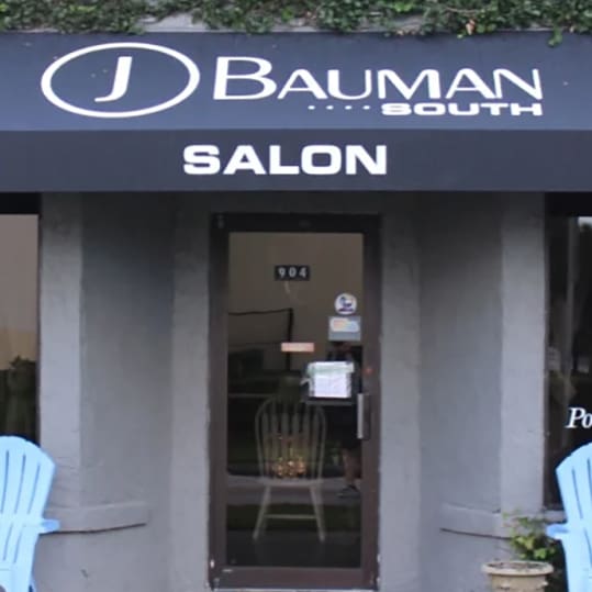 Entrance to bauman salon, featuring a dark blue storefront with the salon's logo above the door and two blue chairs flanking the entryway.
